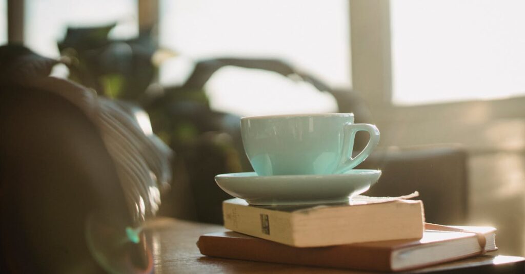 White ceramic cup of tea with plate and worn book with notebook placed on table