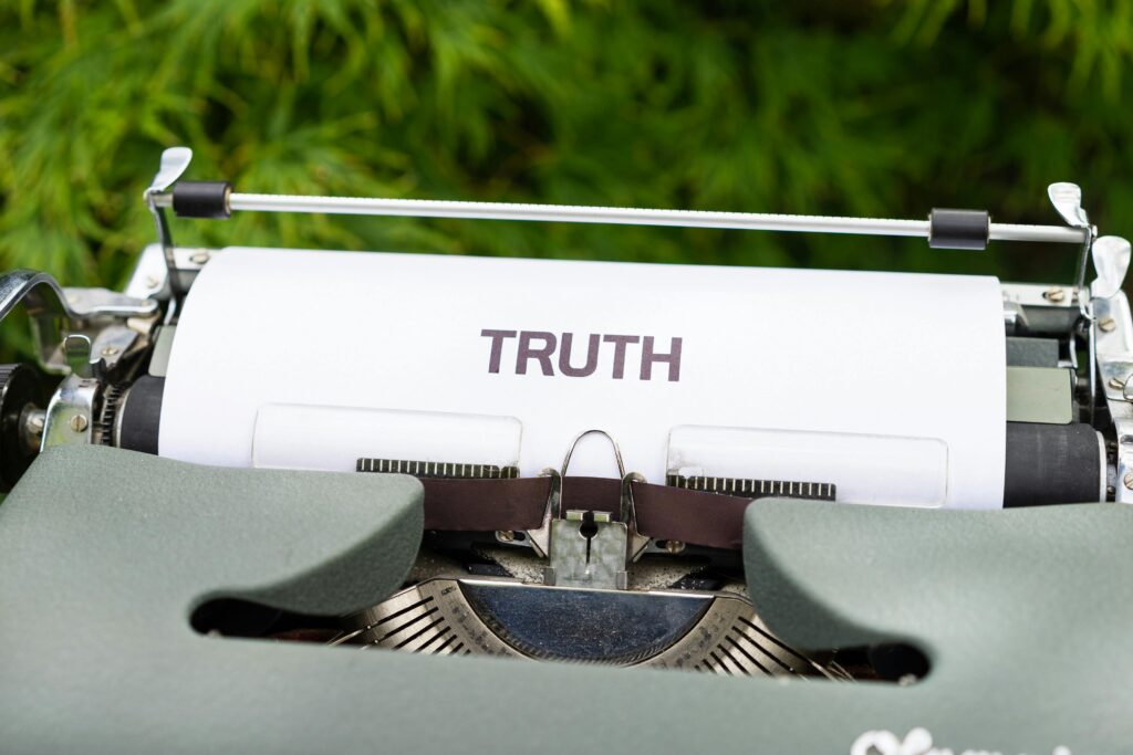 A vintage typewriter features the word 'TRUTH' on paper, set in a natural outdoor background.