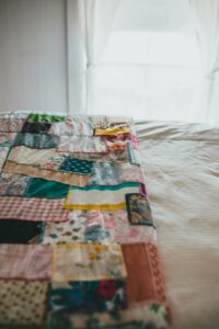pexels-photo-8266835-8266835 A detailed view of a colorful, handmade patchwork quilt draped over a bed in a softly-lit room.